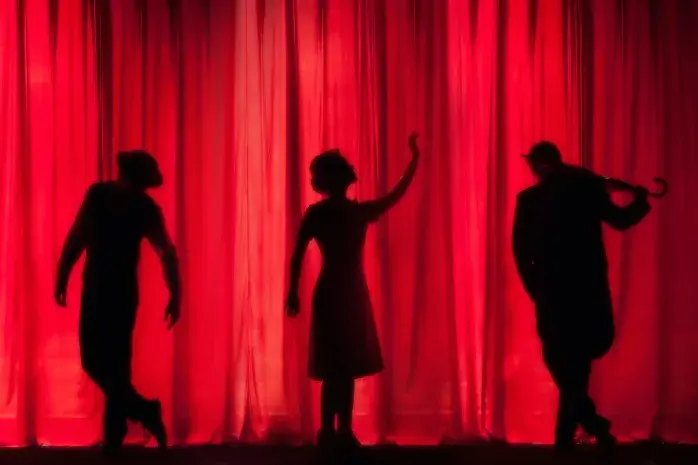 Três sombras humanas num palco com fundo vermelho